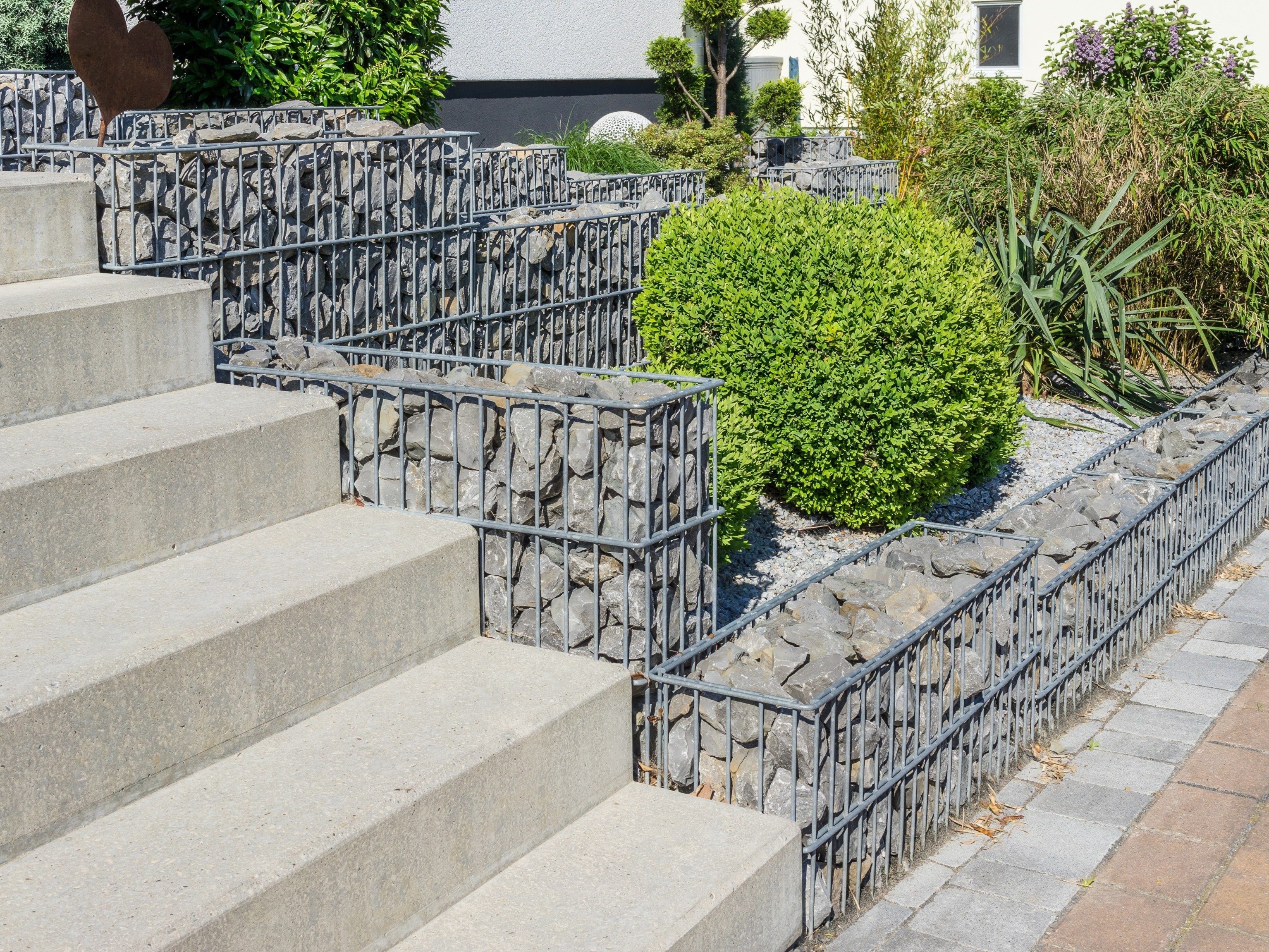 Gabion baskets filled with rocks line garden steps, creating a modern, natural retaining wall and landscaping feature.