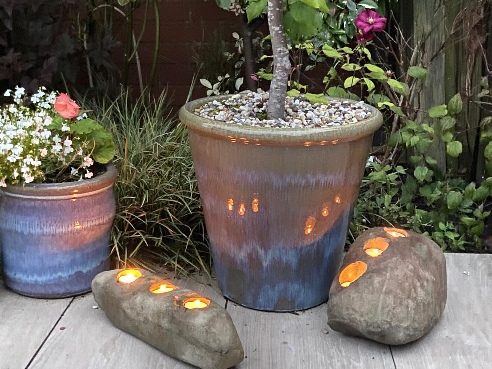 Three-hole decorative candle stones with lit tealights, resting on wooden planks, alongside potted plants.