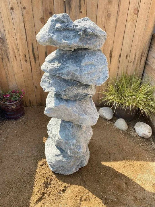 Large green granite water feature, 1000mm tall, stacked on sand and accented by decorative rocks and plants.
