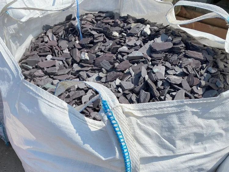 Plum slate chippings for pond edging with pieces of white stone, inside a white sack.