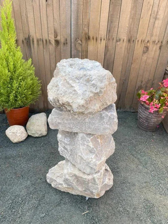 Small grey limestone water feature by unknown vendor, stacked in a backyard setting.