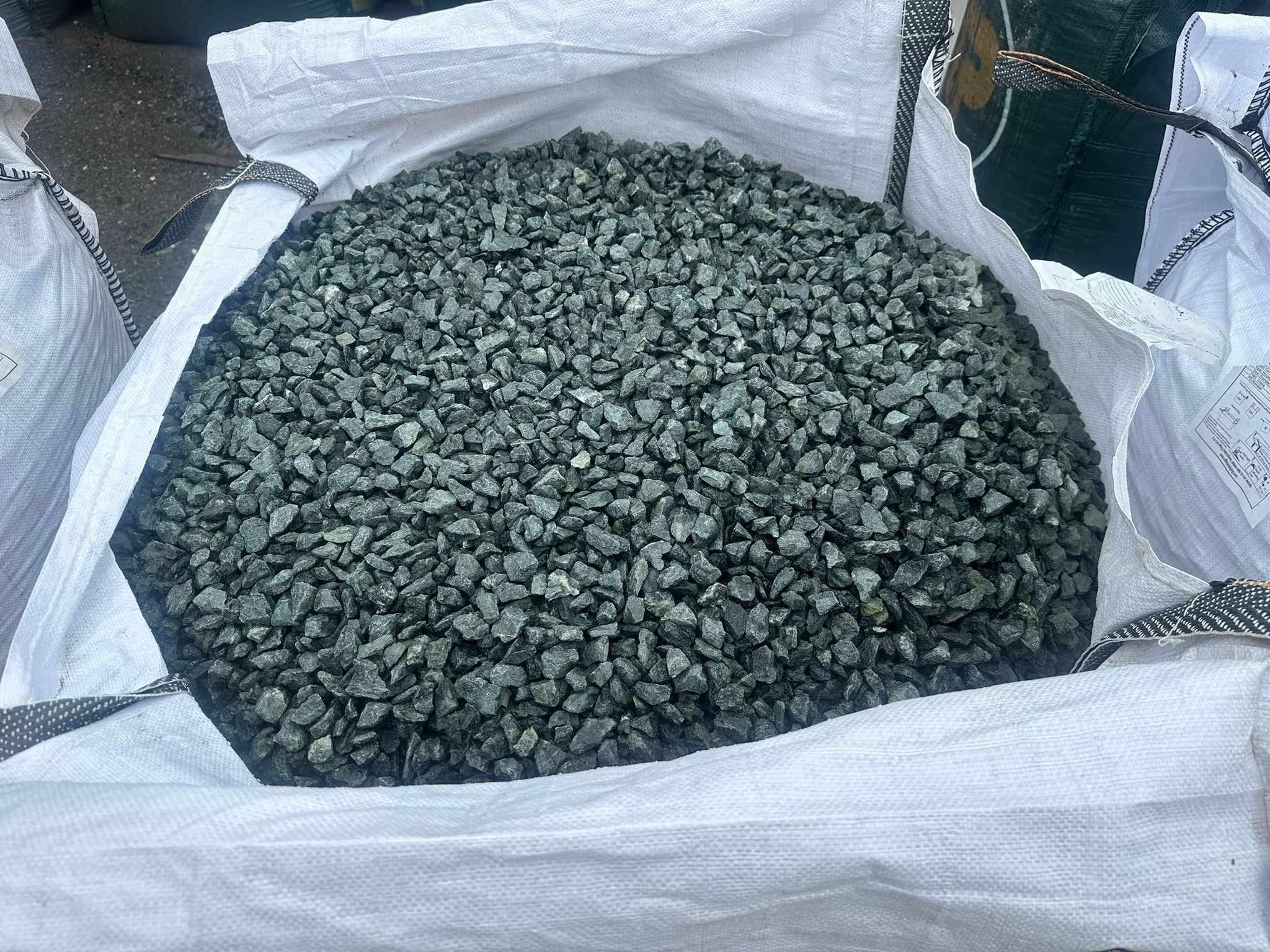 Green granite chippings for gardens inside a white woven bag.