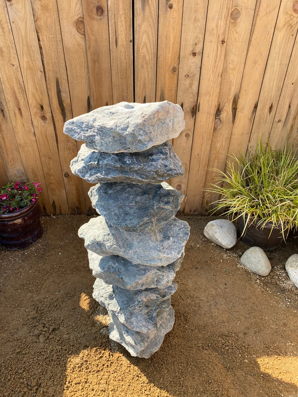 Medium green granite water feature from an unknown vendor, stacked with seven stones in outdoor setting.