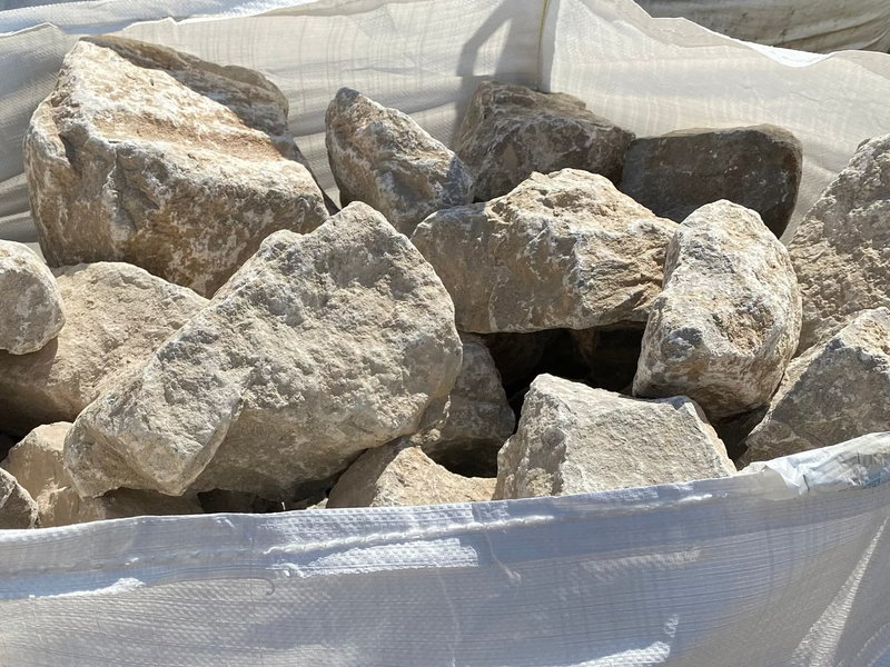 Grey limestone rockery stones for gardens with rough textures in a white bag.