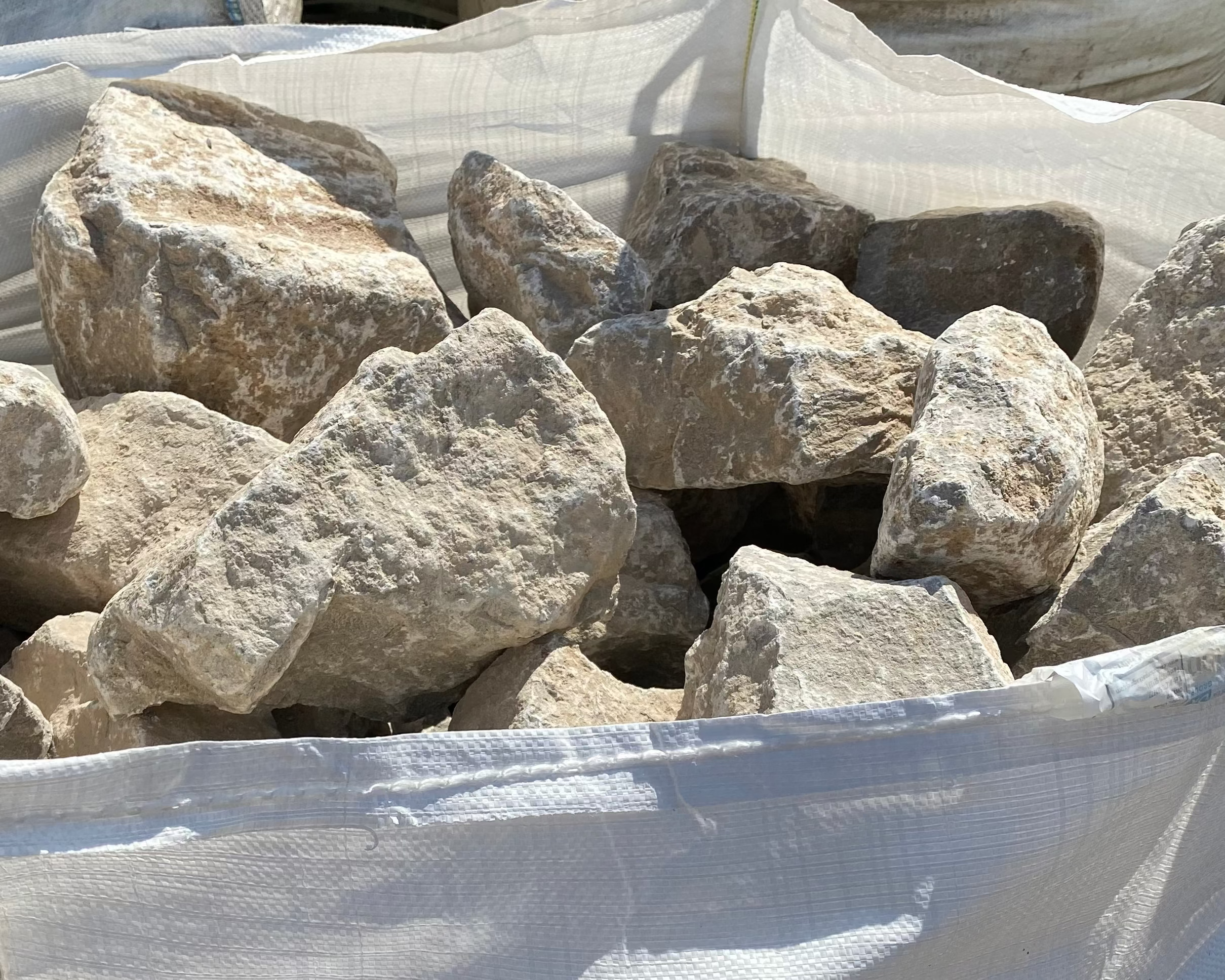 Grey limestone rockery stones for gardens with rough textures in a white bag.