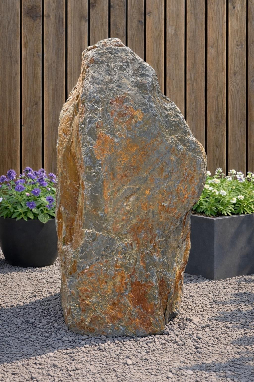 Slate monolith water feature by Water Feature 103, standing on gravel with plant pots in the background.