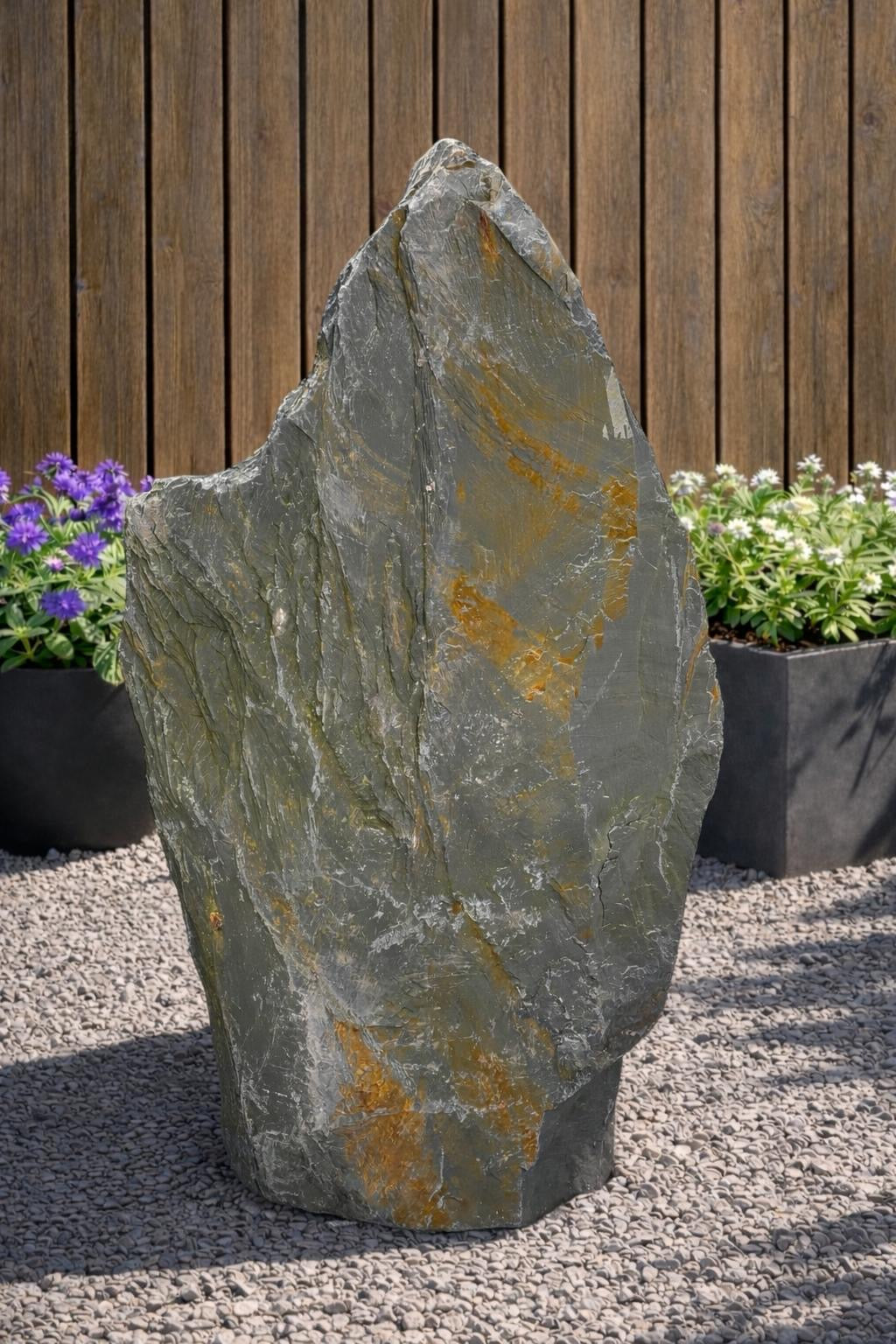 Grey slate monolith standing stone by 121, set amongst gravel and plants.