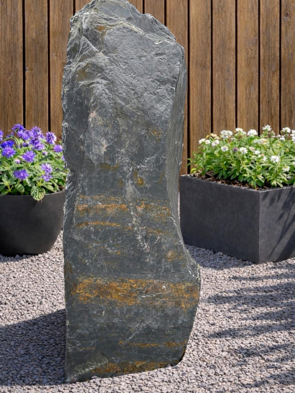 Grey slate monolith standing stone by 132 with gold color striations, set on gravel.