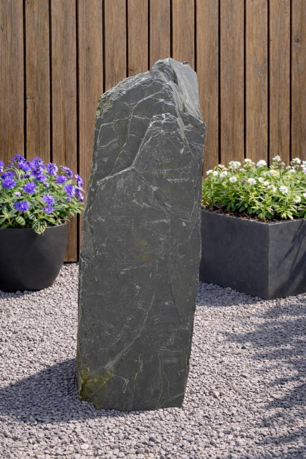 Gray slate monolith water feature from Water Feature with a rough, textured surface sitting on small gravel.