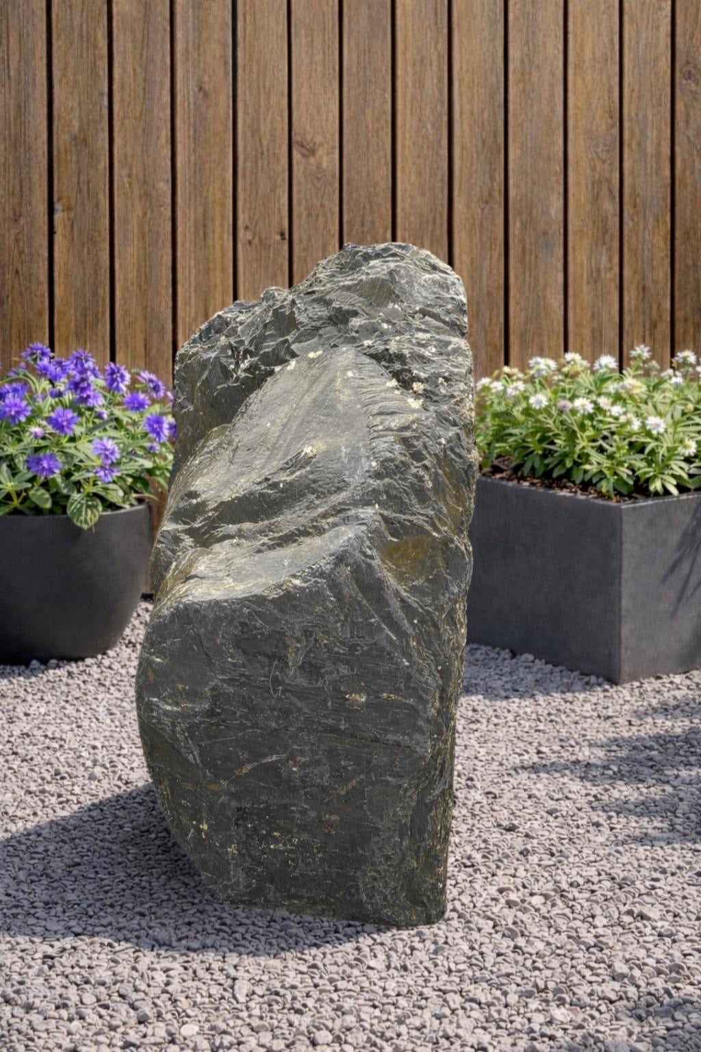 Grey slate monolith standing stone by 134, displayed outdoors with plants and gravel.