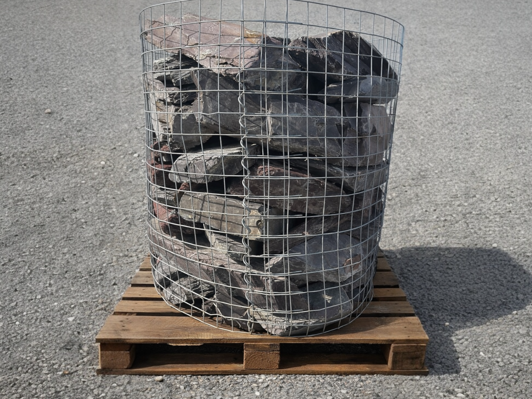 Plum slate gabion stones for gabion baskets, arranged in a wire cage and sitting on a wooden pallet.