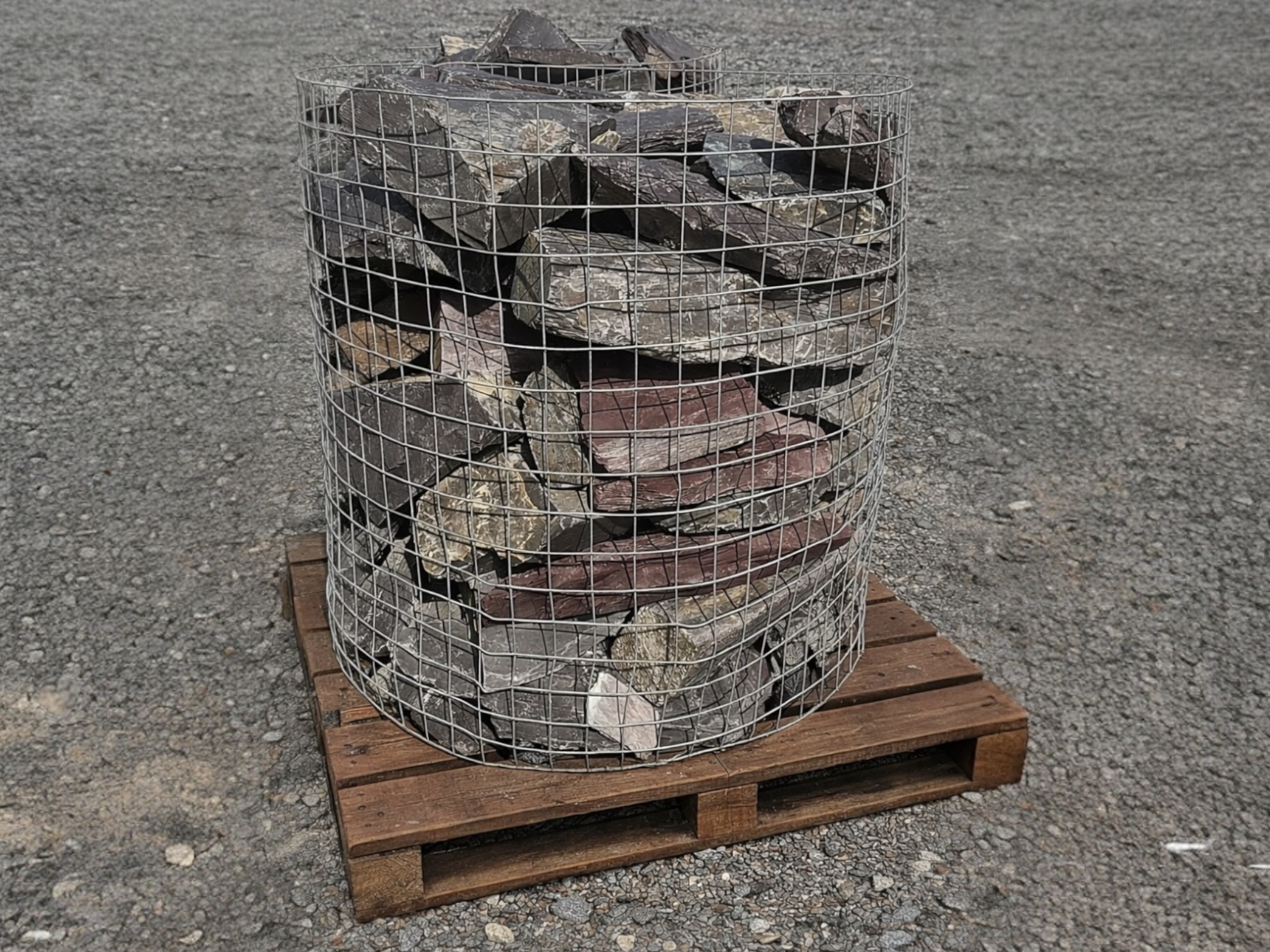 Plum slate decorative pond stones from Dees of a variety of shapes, contained within a wire cage on a wooden pallet.