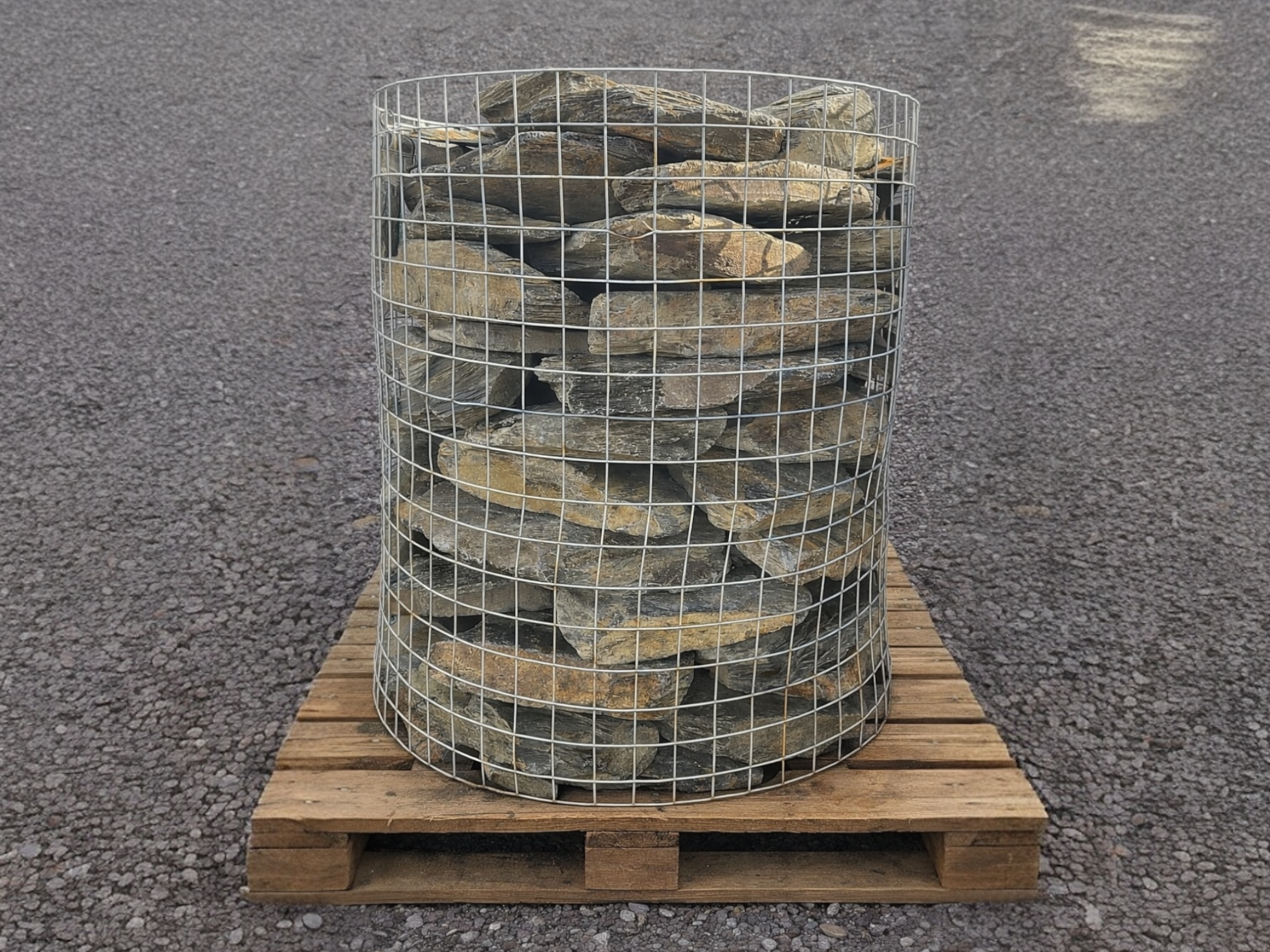 Rustic grey slate gabion stones for gabion baskets inside a silver wire container on a wooden pallet.