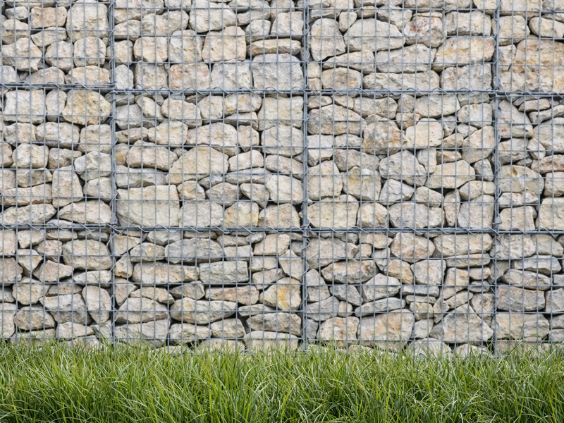 Light limestone gabion stones for gabion baskets, with wire mesh, creating a wall texture, and grass visible along the bottom.