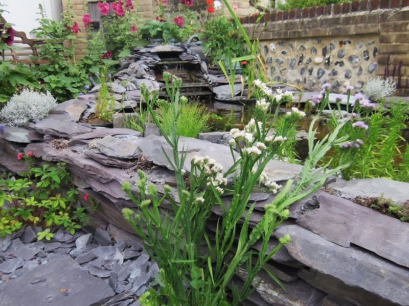 Decorative pond stones of plum slate with layering textures near a pond with foliage.