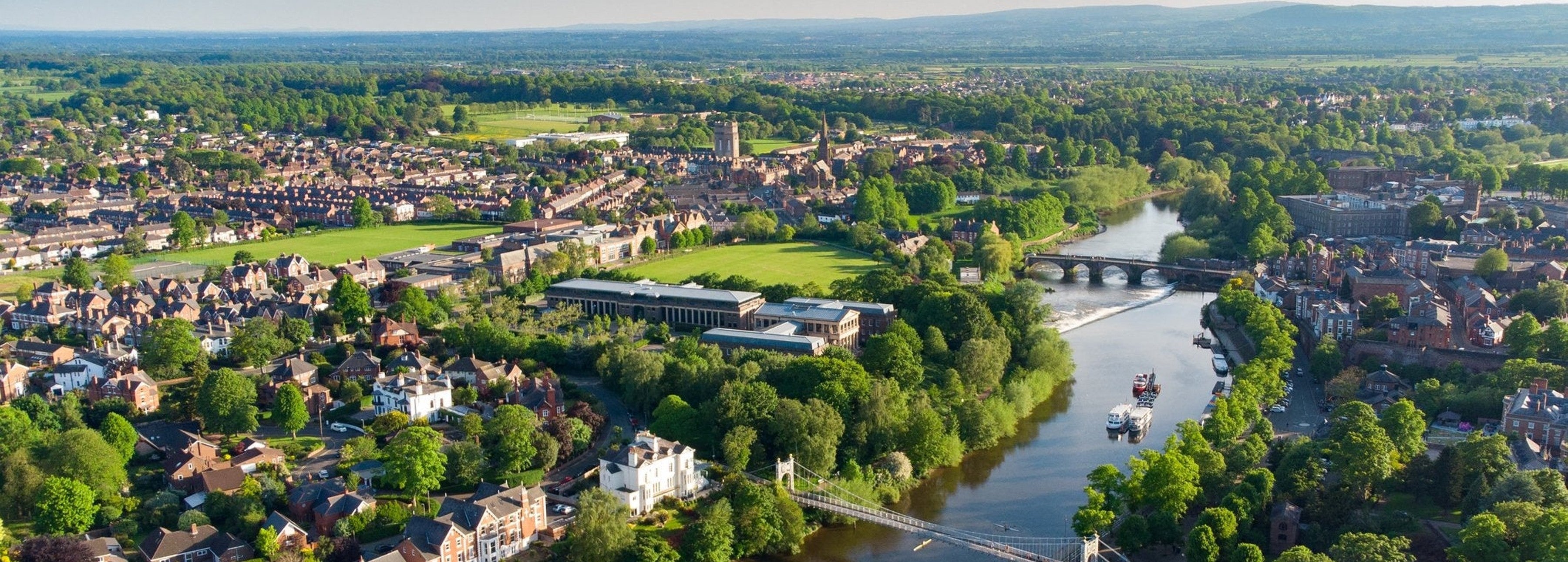 Aerial view of a city with a river running through it, surrounded by lush green trees and buildings.