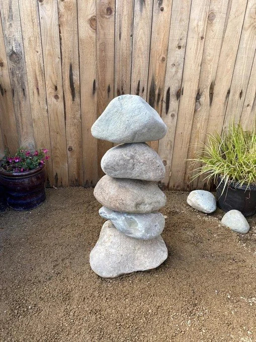 Small stacked stone pebble tower with natural gray stones and sandy texture.