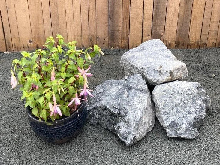 Green granite rockery stones for gardens, with a rough texture, alongside a potted plant and wooden fence.