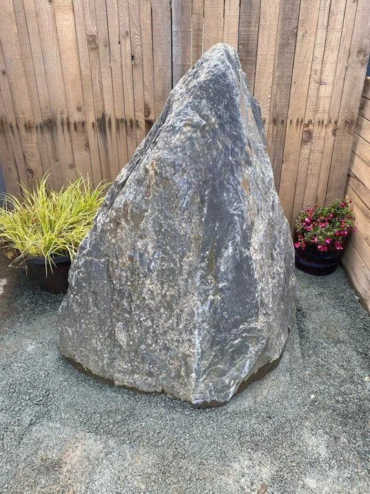 Grey slate monolith feature stone from an unknown vendor with a rough, natural texture standing amongst potted plants.