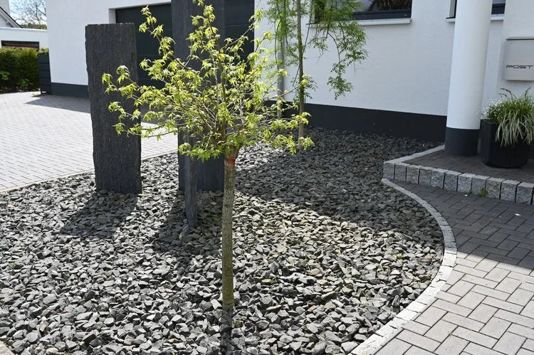 Grey slate mulch in a bulk bag with a rough texture, arranged around small trees and stone pillars.