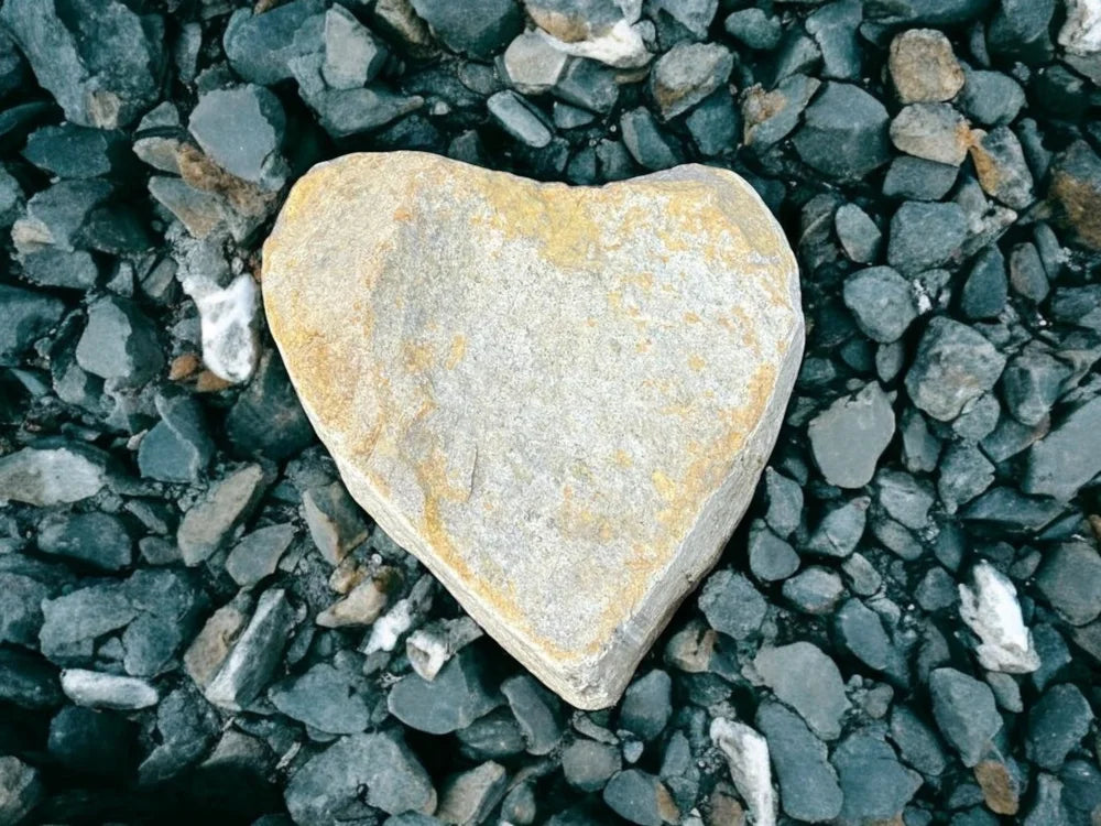Heart boulder made of stone, with yellow accents, surrounded by grey gravel.