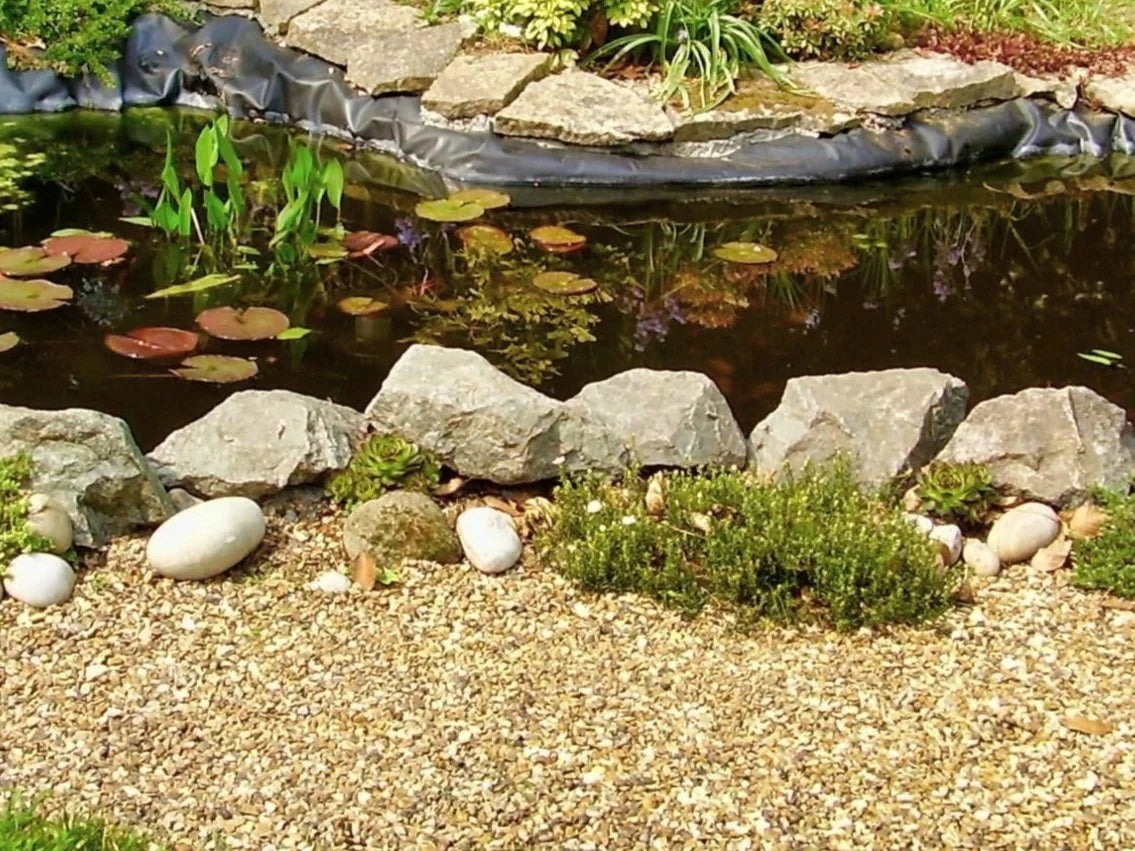 20mm rose quartz pond chippings with light brown gravel background and rocks bordering a pond.