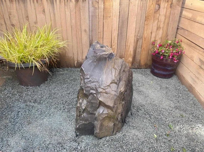 Natural drilled rock water feature RWF02 with a rough, textured surface in a garden setting.