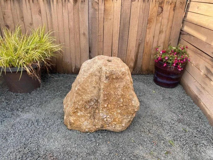 Natural drilled rock water feature by Outdoor Water Solutions with a hole at the top, sitting on gray gravel.