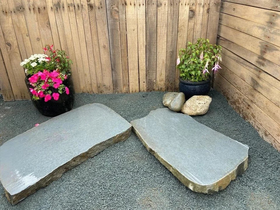 Sawn boulder modern stepping stones for ponds, set on gray gravel near potted plants and a wooden fence.