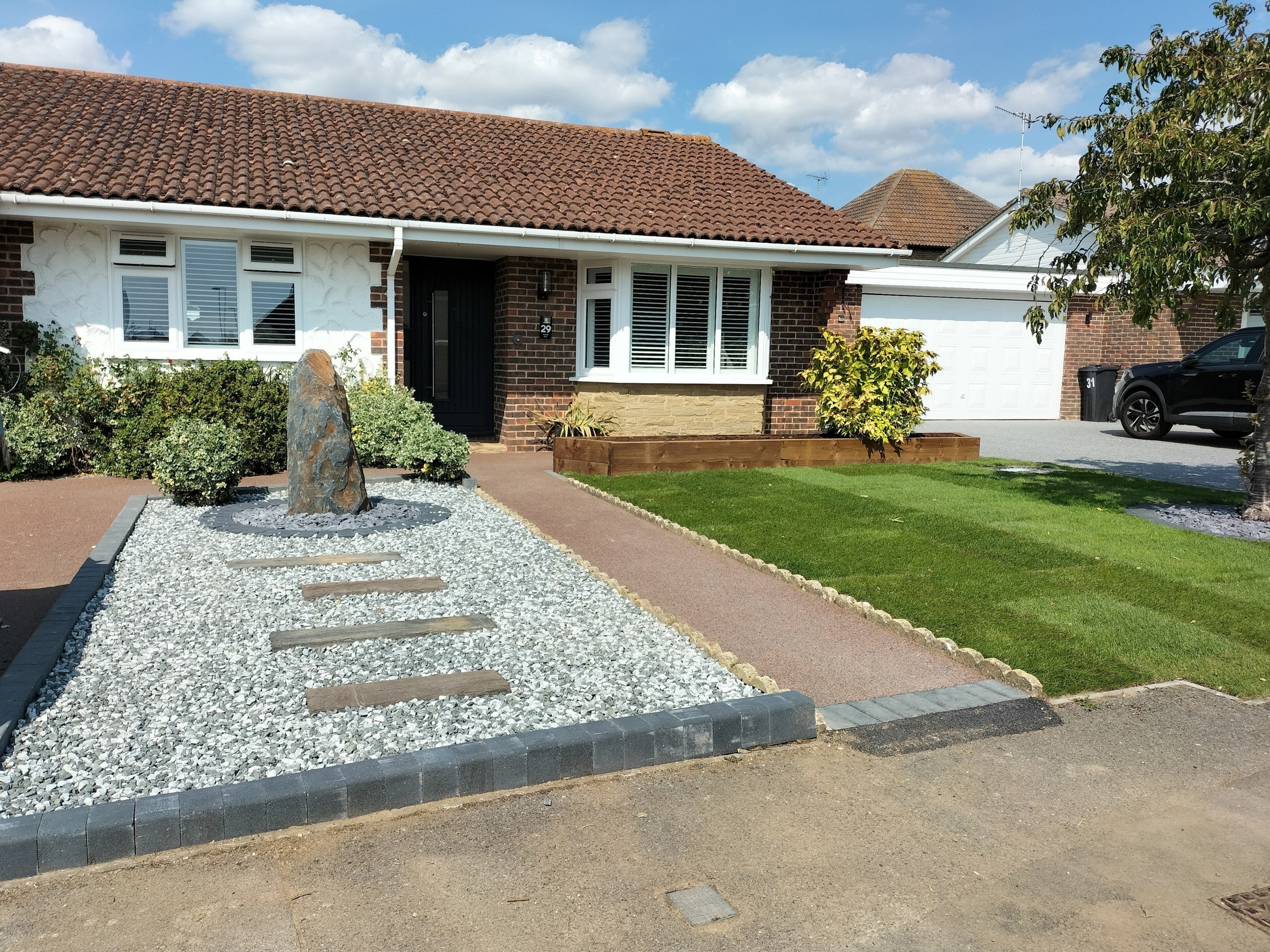 A home's landscaped front yard features a tall, slate monolith water feature amidst decorative stones and lush greenery.