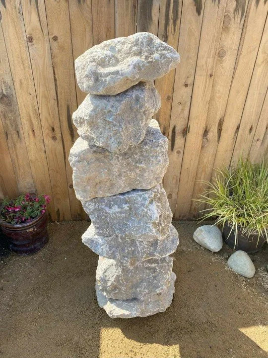 Large grey limestone water feature with stacked rocks, placed in an outdoor garden setting.