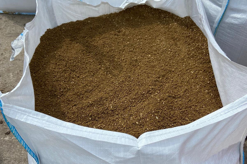 A large, open white bag is filled to the top with loose, dark brown soil or compost. The bag is slightly wrinkled and spilling.

