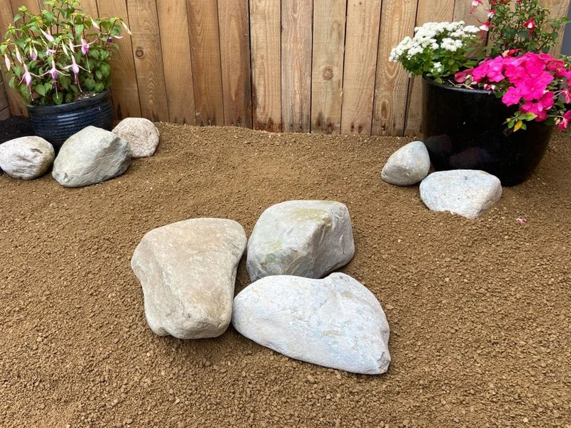 Large decorative garden boulders by [Vendor] scattered across brown gravel in outdoor garden setting.