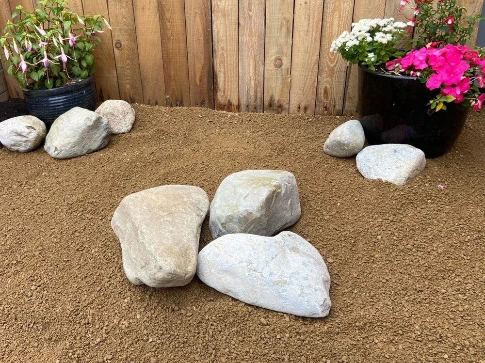 Large decorative garden boulders by [Vendor] scattered across brown gravel in outdoor garden setting.