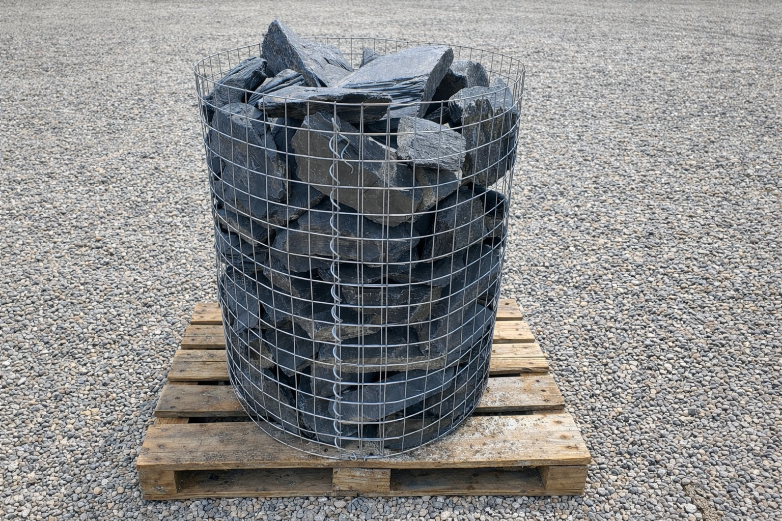 Charcoal grey slate walling stone for landscapes, with wire cage, on a wooden pallet.