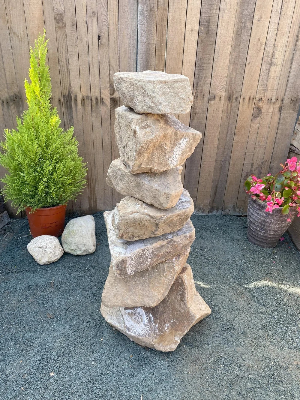 Medium golden granite pyramid stacked stones (800mm) with a rough texture, standing outdoors against a wooden fence.