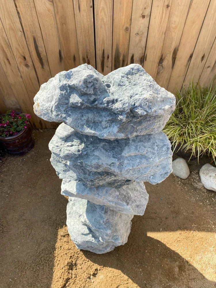 Large green granite water feature from Granite Water Features set against a wooden fence with sandy ground.

