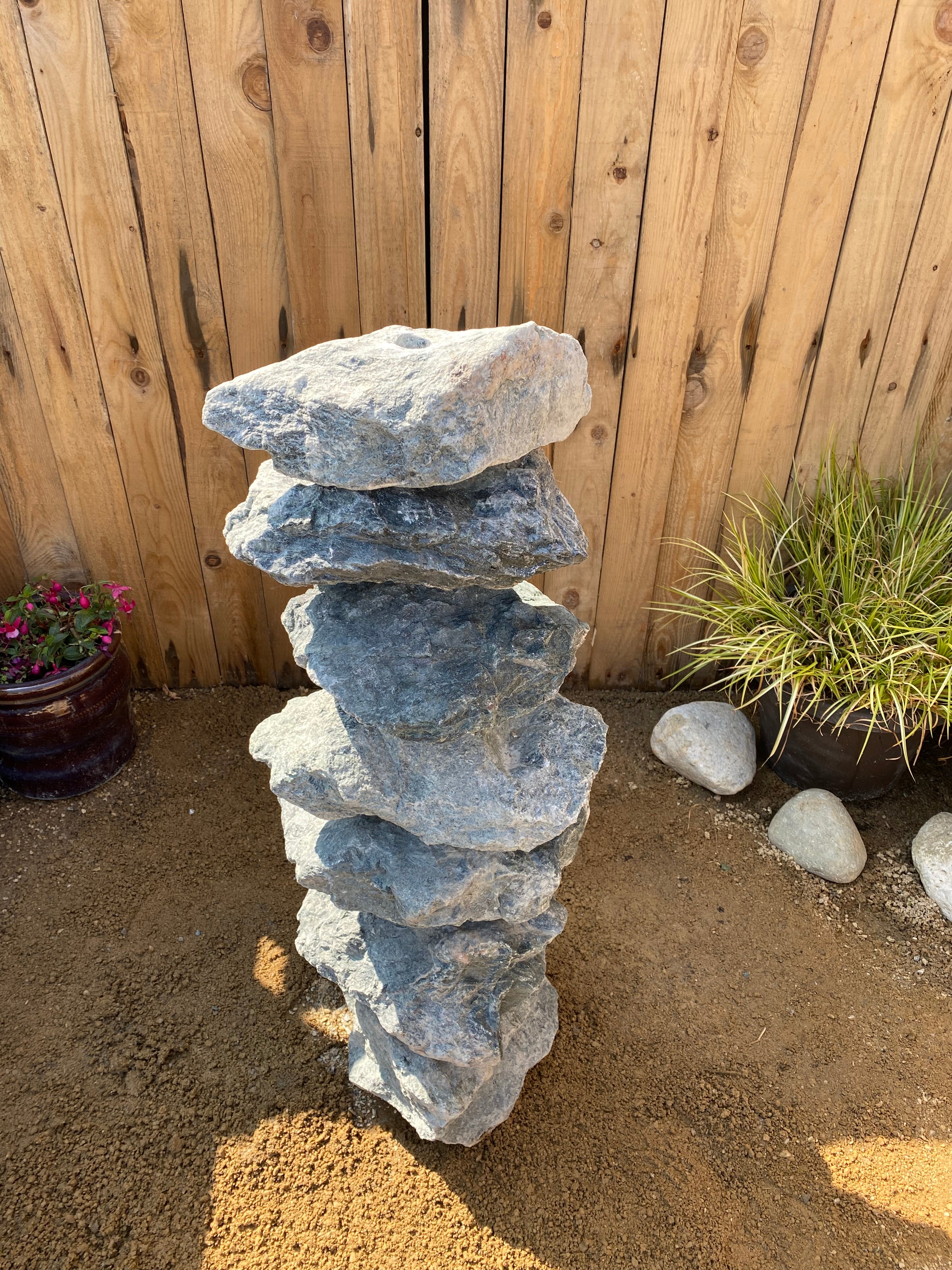 Medium green granite water feature from an unknown vendor, stacked with seven stones in outdoor setting.