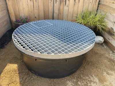 Black water feature kit with metal grate top, surrounded by tan gravel.