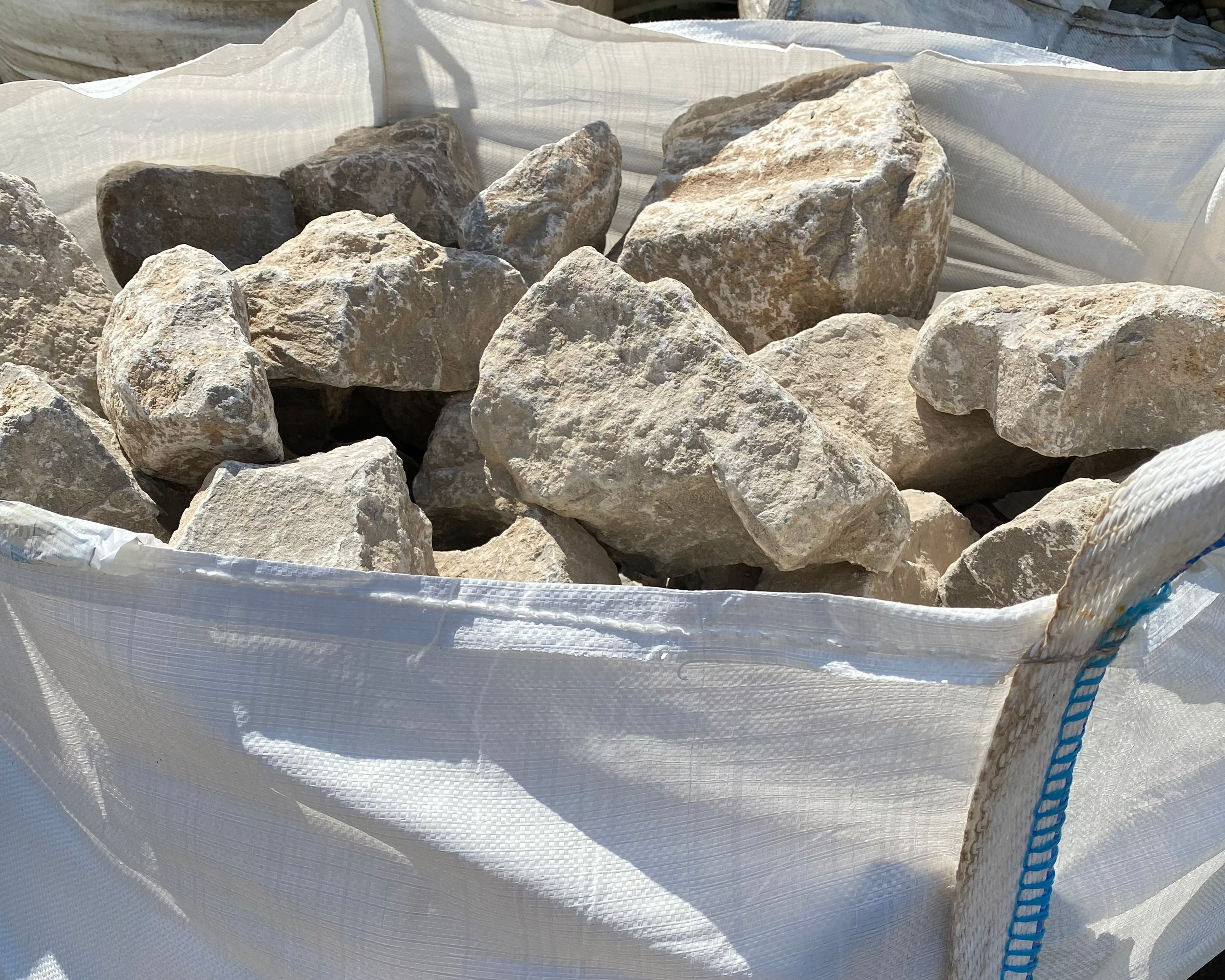 Light limestone gabion stones for gabion baskets with a rough texture in a large white bag.