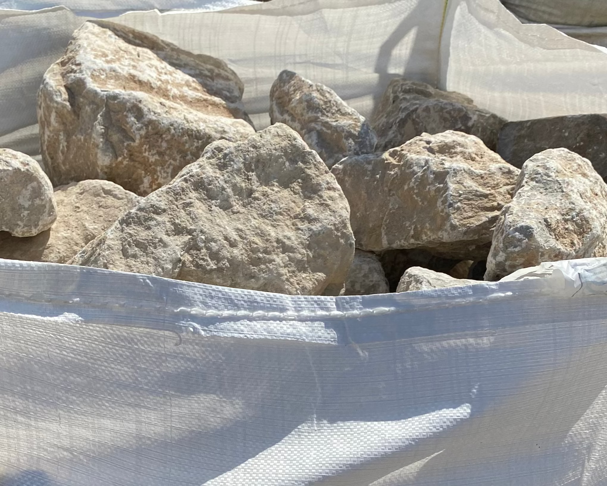Natural limestone walling stone in a bulk bag, showing rough, textured surfaces.