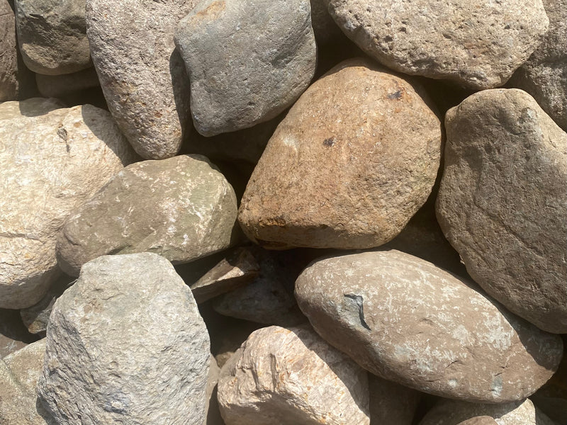 A close-up shows a pile of various-sized, smooth river rocks, mainly tan and gray, creating a textured, natural background.