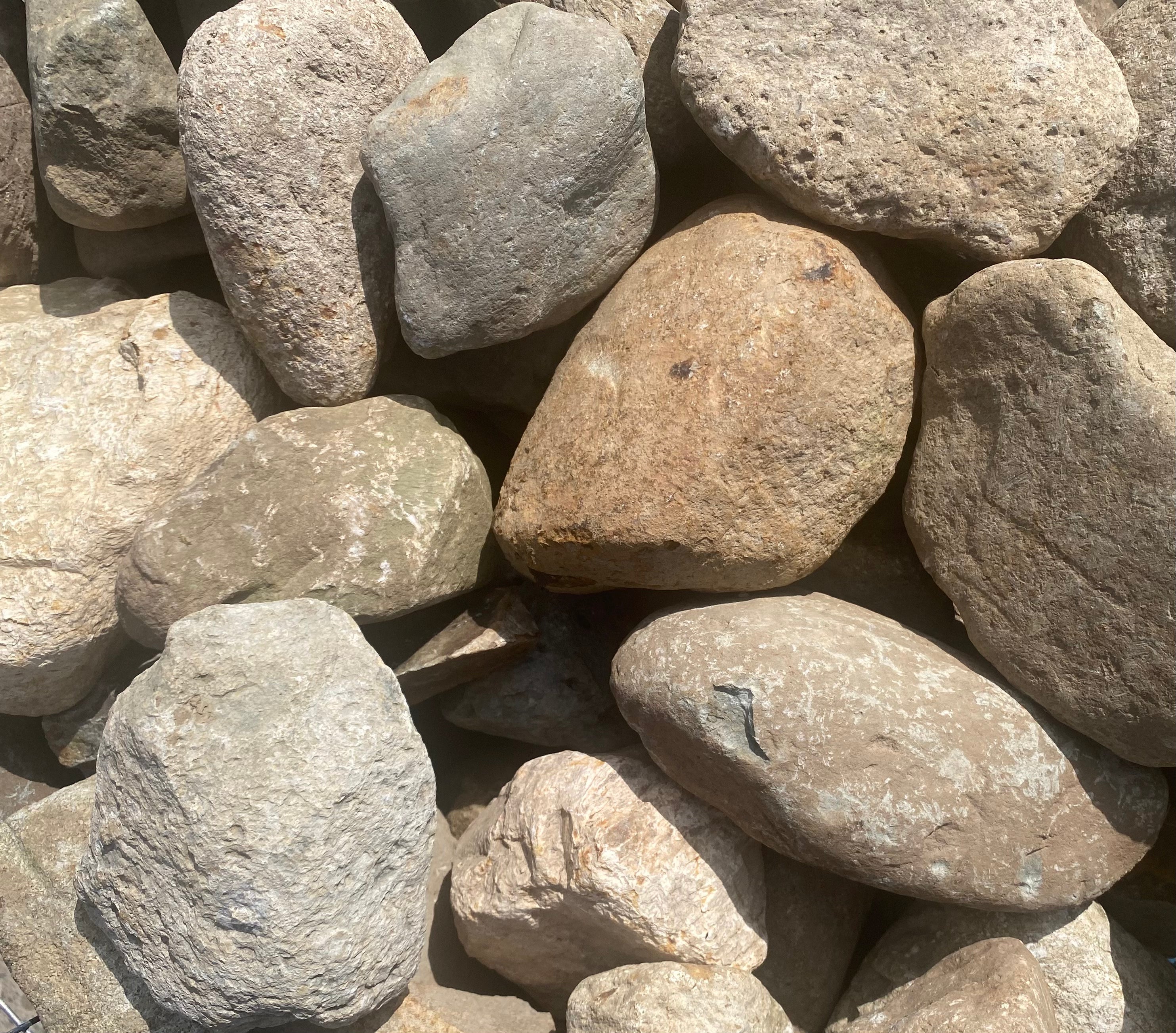 A close-up shows a pile of various-sized, smooth river rocks, mainly tan and gray, creating a textured, natural background.