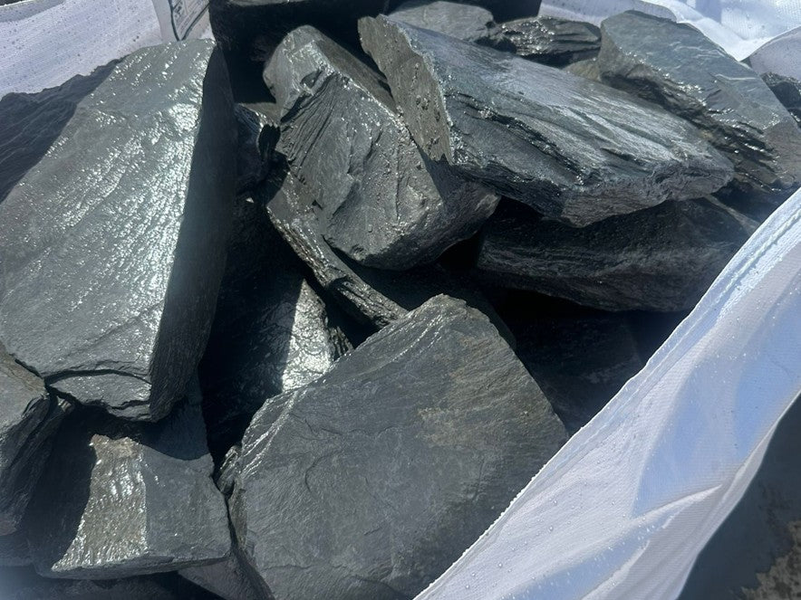 Charcoal slate decorative pond stones close-up, with layered texture, loaded in a white woven bag.