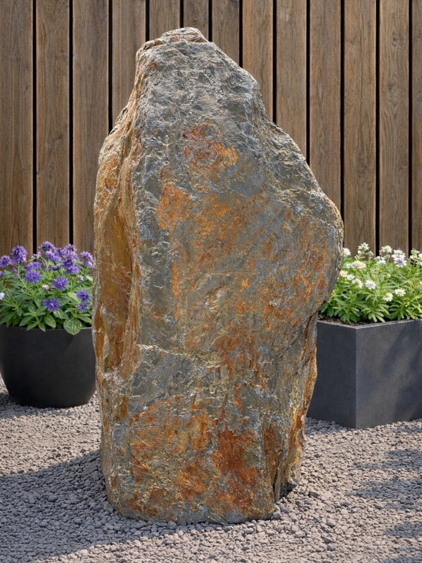 Slate monolith water feature by Water Feature 103, standing on gravel with plant pots in the background.