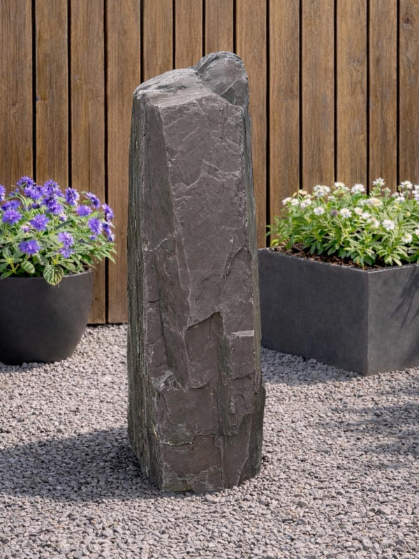 Slate monolith water feature by Water Feature 110, standing tall amongst gravel and potted plants.