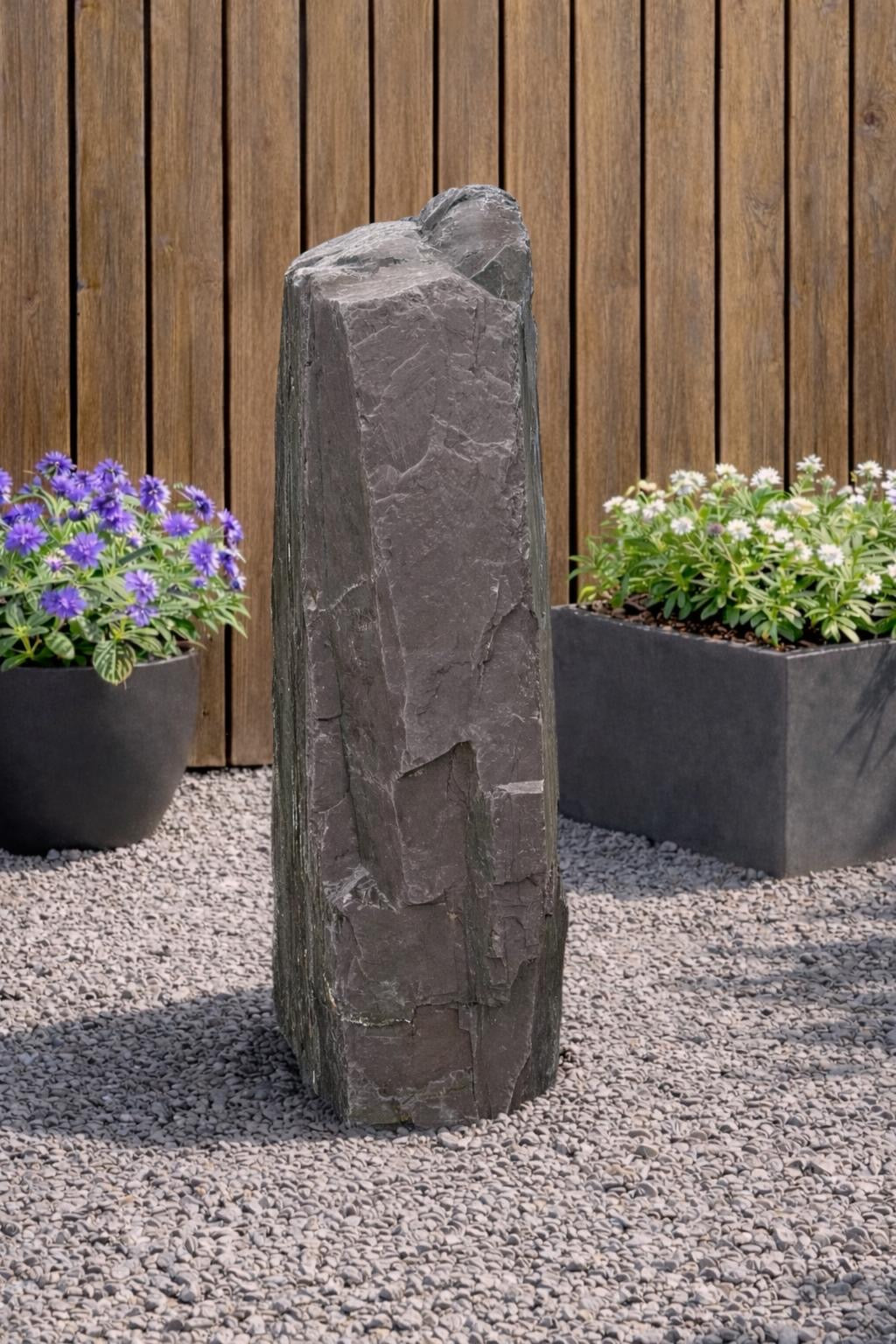Slate monolith water feature by Water Feature 110, standing tall amongst gravel and potted plants.