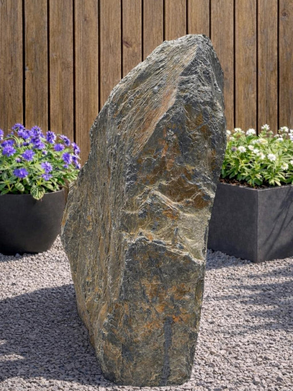 Gray slate monolith by Water Feature 116, with natural rock texture, set amongst light gravel and plants.