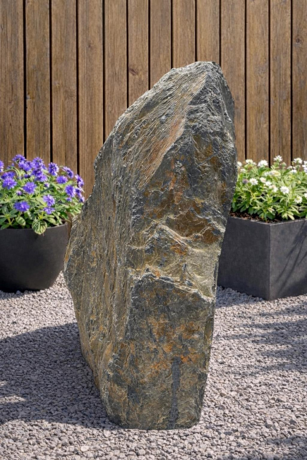 Gray slate monolith by Water Feature 116, with natural rock texture, set amongst light gravel and plants.