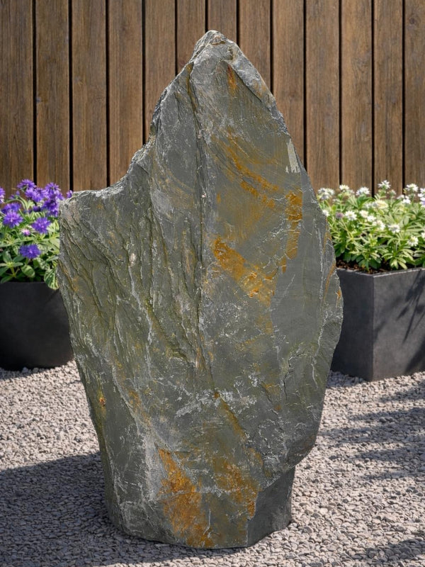 Grey slate monolith standing stone by 121, set amongst gravel and plants.